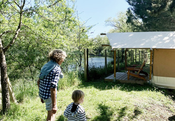 Dos personas caminan hacia una tienda safari llamada Bivouac Comfort en el camping Le Val de Cesse en Francia.