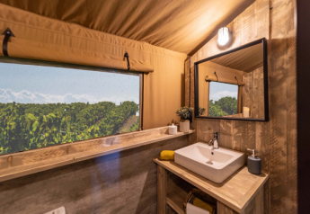 Baño con lavabo y decoración de madera en una tienda safari Glamping Lodge PREMIUM en el camping Le Val de Cesse, Francia.