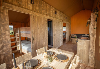 Interior de la tienda safari Glamping Lodge PREMIUM en el camping Le Val de Cesse, Francia, con comedor.