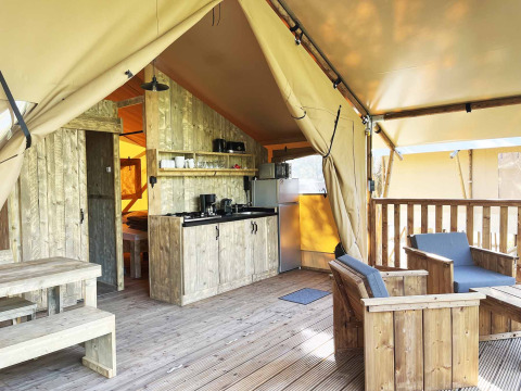 Interno di una tenda safari con mobili in legno, angolo cottura e zona salotto esterna su veranda.