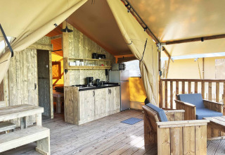 Interno di una tenda safari con mobili in legno, angolo cottura e zona salotto esterna su veranda.