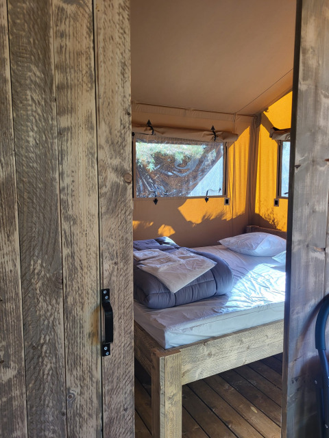 Vista attraverso una porta di legno su un letto accogliente all'interno di una tenda safari con pareti gialle.