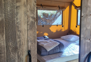 Vista attraverso una porta di legno su un letto accogliente all'interno di una tenda safari con pareti gialle.
