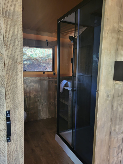 Ingresso al bagno di una tenda safari con pannelli in legno, box doccia e finestra panoramica.