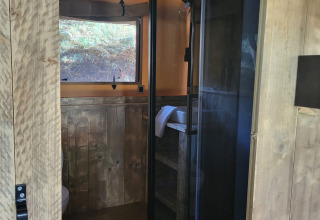 Ingresso al bagno di una tenda safari con pannelli in legno, box doccia e finestra panoramica.