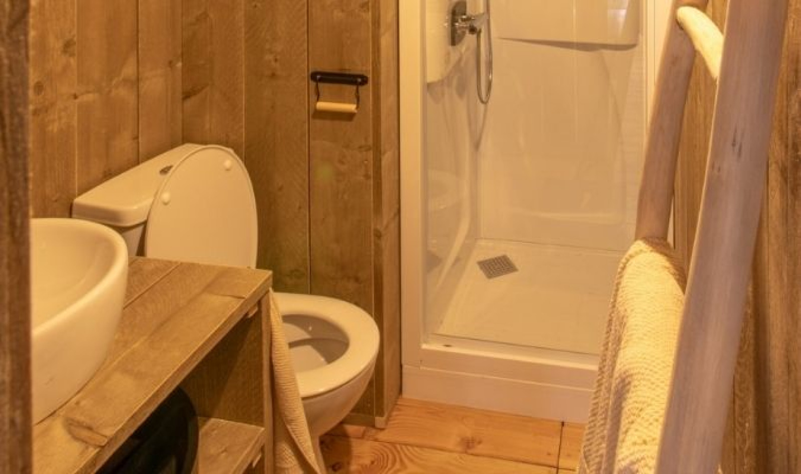 Badkamer in een glamping lodge met houten wanden, toilet, wastafel en douche op een camping in Frankrijk.