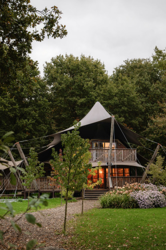 Tienda de glamping safari Hacienda en Resort de Parel, Países Bajos, rodeada de árboles y flores verdes.