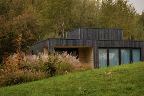 Moderne villa van donker hout bij Resort de Parel in Nederland, omgeven door gras en groene bomen.