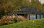 Villa moderne en bois sombre au Resort de Parel, Pays-Bas, entourée de gazon et d’arbres verdoyants.