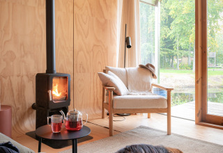 Intérieur chaleureux du Wrap house avec poêle, fauteuil, thé et chien endormi à Resort de Parel, Pays-Bas.