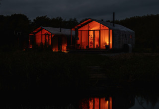 Vista nocturna de Wrap House con sauna y bañera en Resort de Parel, Países Bajos, reflejada en el agua.