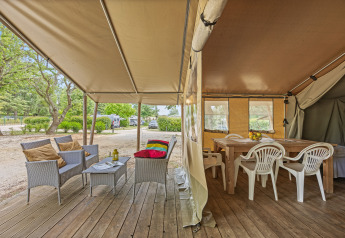 Interno ed esterno della tenda safari Harmony con zona salotto accogliente, tavolo da pranzo e vista naturale.