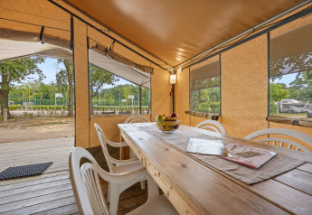 Zona pranzo nella Safaritent Harmony con tavolo in legno, sedie bianche e vista panoramica sulle aree esterne.