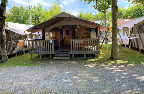 Photo d'une tente safari avec une véranda en bois et des sièges extérieurs, entouré d’arbres en camping.