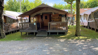 A photo of a safari tent with a wooden porch and outdoor seating, surrounded by trees at a campsite.