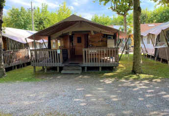 A photo of a safari tent with a wooden porch and outdoor seating, surrounded by trees at a campsite.