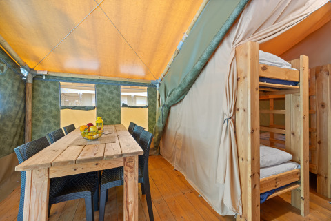 Vue intérieure de la Safaritent Relax avec table en bois, chaises et lits superposés pour un séjour confortable.