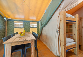 Binnenzicht van Safaritent Relax met houten tafel, stoelen en stapelbed, perfect voor een gezellige vakantie.