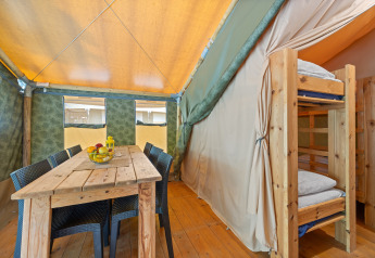 Vista interna della Safaritent Relax con tavolo in legno, sedie e letti a castello per una vacanza confortevole.