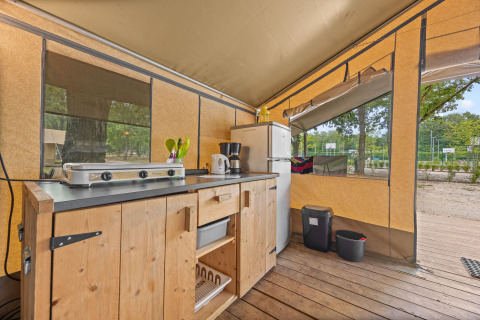 Küche im Safaritent Harmony mit Herd, Kühlschrank und Holzschrank, ideal für komfortables Camping.