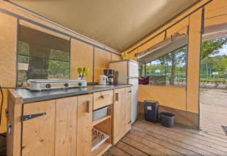 Küche im Safaritent Harmony mit Herd, Kühlschrank und Holzschrank, ideal für komfortables Camping.