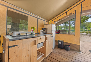 Kitchen area inside Safaritent Harmony with stove, fridge, and wooden cabinet, ideal for luxury camping.