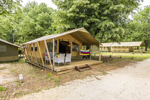 Outdoor view of Safaritent Harmony with deck and patio chairs, nestled among trees in a natural setting.