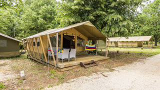 Vista exterior de la Safaritent Harmony con terraza y sillas, rodeada de árboles en un entorno natural.