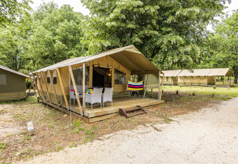Buitenaanzicht van Safaritent Harmony met terras en stoelen, omgeven door bomen in een natuurlijke omgeving.