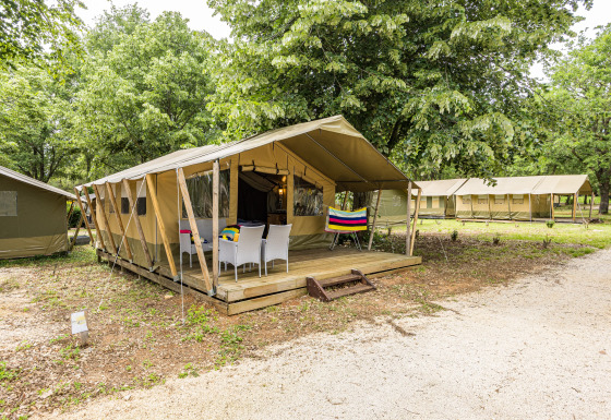 Outdoor view of Safaritent Harmony with deck and patio chairs, nestled among trees in a natural setting.