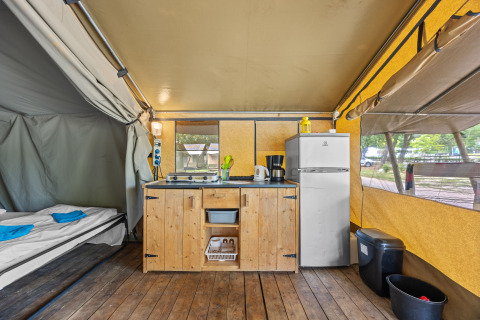 Innenraum des Safaritent Harmony mit Küchenzeile, Kühlschrank und Bett unter einem großen Zelt.