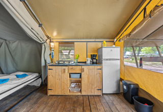 Intérieur de la Safaritent Harmony avec kitchenette, réfrigérateur et lits dans une grande tente.