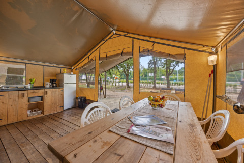 Innenraum des Safaritent Harmony mit Holztisch, Stühlen, Küchenzeile und Blick ins Grüne durch offene Fenster.