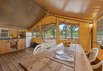 Interior de la Safaritent Harmony con mesa de madera, sillas, cocina y vista a la naturaleza exterior.