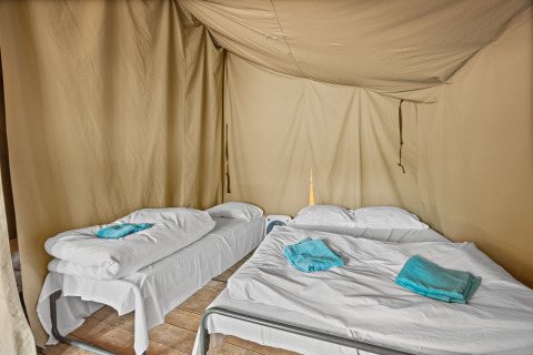 Intérieur de la tente safari Harmony avec un lit simple et un lit double, draps blancs et serviettes bleues.