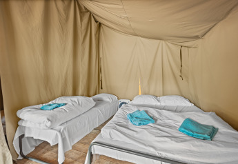 Vista interna della Safaritent Harmony con un letto singolo e uno matrimoniale, biancheria e asciugamani azzurri.