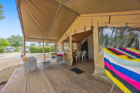 Tente safari Harmony avec terrasse en bois, fauteuils confortables, serviettes colorées et vue sur le camping.