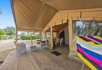 Tenda safari Harmony con veranda in legno, sedie confortevoli, asciugamani colorati e vista sul campeggio.