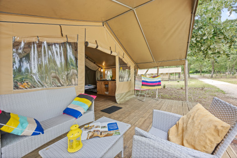 Véranda de tente safari Safaritent Harmony avec assises confortables, coussins colorés, vue sur la nature.