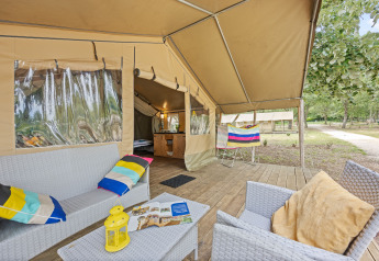 Veranda della tenda safari Safaritent Harmony con comode sedute, cuscini colorati e vista sul verde.