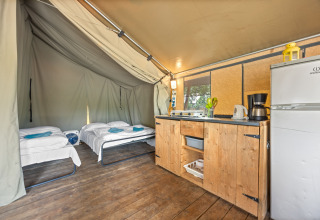 Binnenzicht van Safaritent Harmony met twee bedden, een kitchenette, houten vloer en koelkast op camping.