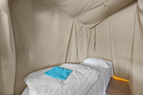 Single bed with white bedding and blue towel inside the Safaritent Harmony safari tent interior.