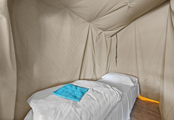 Letto singolo con lenzuola bianche e asciugamano blu all'interno della tenda safari Safaritent Harmony.