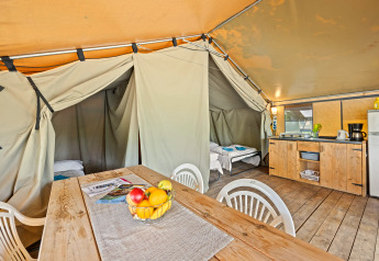 Interieur van een Safaritent Harmony met houten tafel, keukenblok, plastic stoelen en twee slaapruimtes.