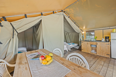 Innenansicht eines Safaritent Harmony mit Holztisch, Stühlen, Küche, Kühlschrank und zwei Schlafräumen.