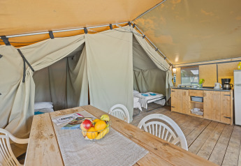 Binnenkant van de Safaritent Harmony met een houten tafel, keuken, plastic stoelen en twee slaapgedeeltes.