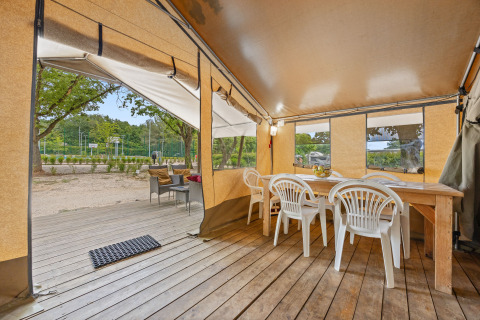 Inside view of Safaritent Harmony showing a wooden table, white chairs, and a deck facing the outdoors.