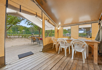 Interno della Safaritent Harmony con tavolo in legno, sedie bianche e terrazza che si apre sulla natura.