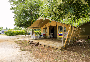 Safaritent Harmony met overdekt houten terras, tuinmeubilair en groene bomen op de camping.