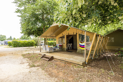Tenda safari Harmony con terrazza in legno coperta, sedute all'aperto e verde in campeggio.